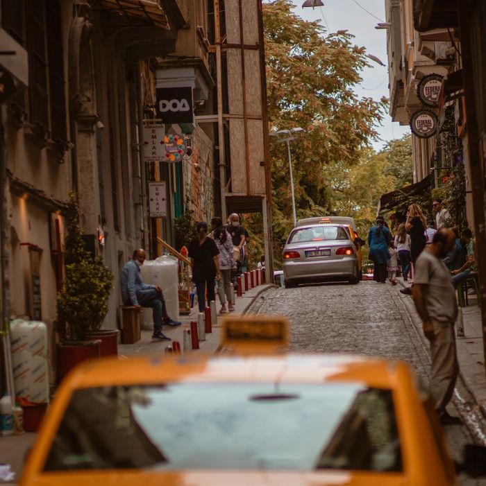 Lively city street scene with taxis and people on a cobblestone road lined with shops.