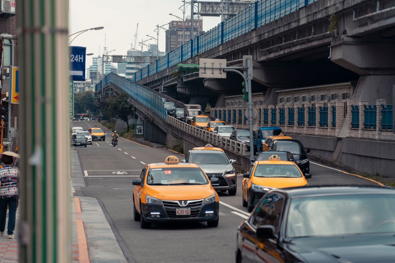 Yellow taxis and vehicles navigating an urban street under an overpass.